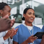 Healthcare workers in scrubs smiling and using a tablet together.