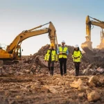 FIFO workers in high-visibility safety gear inspecting a mining site with excavators.