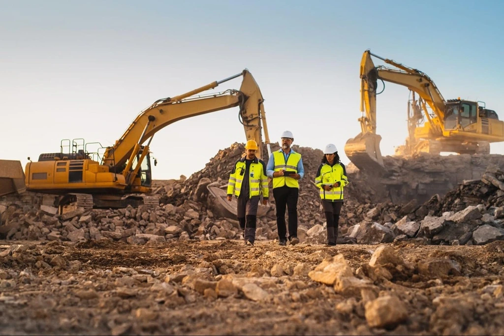 FIFO workers in high-visibility safety gear inspecting a mining site with excavators.