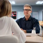 Professional meeting with a man wearing glasses discussing ideas with a colleague in an office.